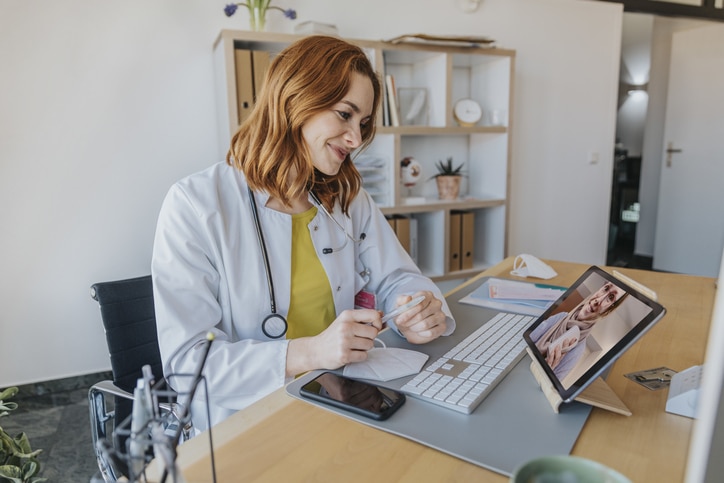 Doctor listening to patient on video call over digital tablet while sitting at office Medical abortion by phone